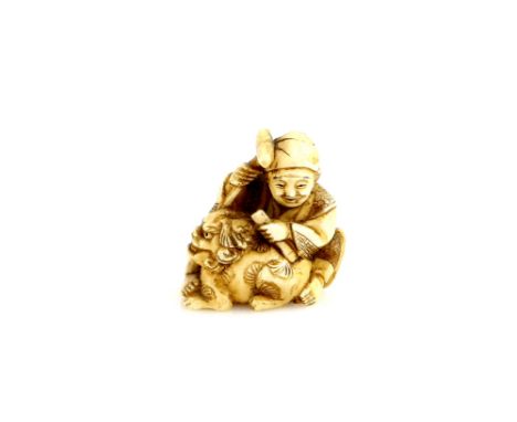 A stained ivory netsuke carved as a seated artisan sculpting a karashishi with hammer and chisel, 20th CenturyProvenance: The