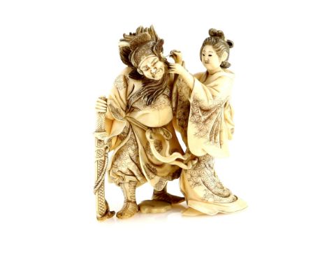 A stained ivory okimono, carved a standing Bijin assisting Emma-O to clean his left ear, 9 cm high, 19th or 20th CenturyProve