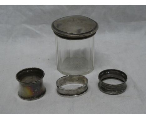 A small silver oval napkin ring with engine turned decoration, two other circular silver napkin rings and a silver topped gla