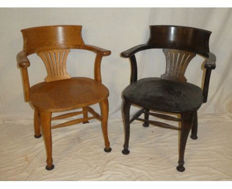 A pair of Edwardian oak office chairs with pierced splat backs and shaped seats on scroll-shaped legs (one dark and one light