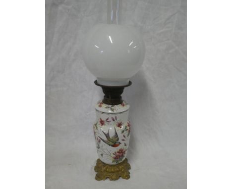 An old enamelled and brass oil lamp with detachable font on iron base with opaque glass shade