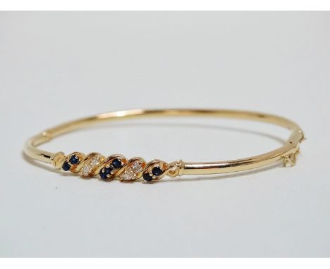 A diamond and sapphire bangle - the crossover setting in 14ct yellow gold, weight 5g. 