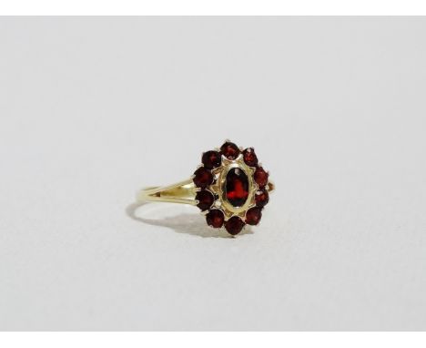 A ruby cluster ring - the oval cut central stone within a further band of circular cut rubies, set on an 18ct yellow gold ban