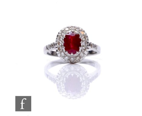 An 18ct hallmarked white gold ruby and diamond cluster ring, central oval ruby, length 8mm, claw set to a sixteen stone diamo