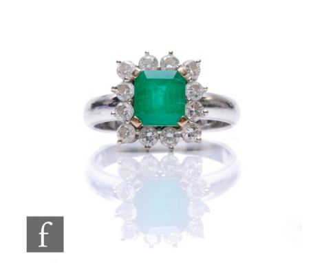 An 18ct white gold emerald and diamond cluster ring, square cut emerald, width 7mm, within a border of twelve brilliant cut d
