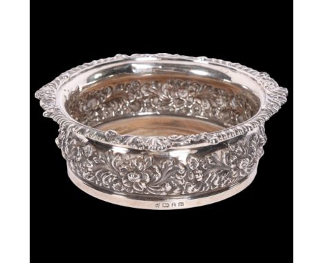 A large George V silver wine coaster, having ornate repousse floral decoration and turned wood base, diameter 17cm, height 5.
