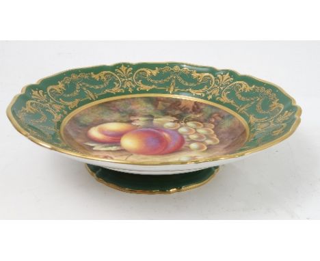 A Royal Worcester tazza, decorated to the centre with a panel of hand painted fruit, by Ayrton, to a deep green and gilt bord