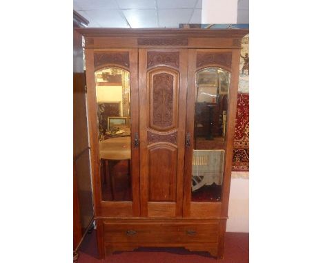 An Art Nouveau wardrobe, with central carved panel flanked by two mirrored cupboard doors with bevelled plates, raised on bra