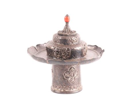 A Sino Tibetan silver metal cup stand and cover, 19th century, the cover with coral coloured glass finial above panels of aus