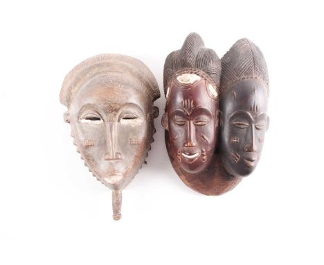 A Baule Janus mask, Mblo, Ivory Coast, each with inear carved coiffure, above a single braid on the right and double braid on