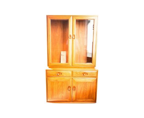 An Ercol golden dawn light elm two-section display cupboard. With two glazed doors above a base with blind panel doors. 92 cm