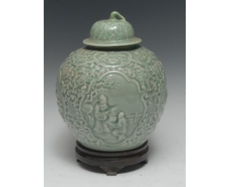 A Chinse celadon ovoid wine jar and cover, moulded in relief with four reserves of traditional figures below a ruyi frieze, d