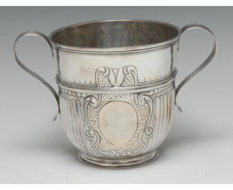 A Queen Anne Britannica silver half-fluted porringer, chased with a vacant leafy scroll and scale cartouche, scroll handles, 