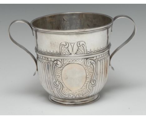 A Queen Anne Britannica silver half-fluted porringer, chased with a vacant leafy scroll and scale cartouche, scroll handles, 