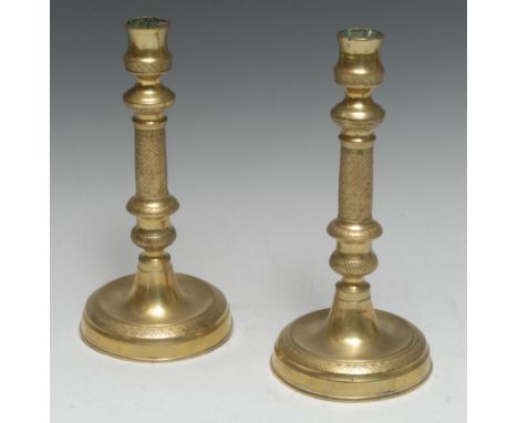 A pair of French Empire gilt brass table candlesticks, urnular sconces, engine turned with flowerhead diapers, dished circula