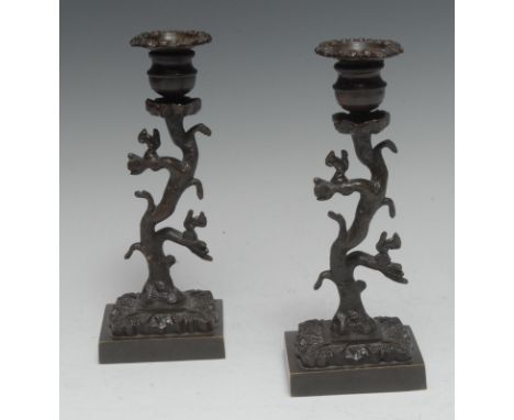 A pair of Regency brown patinated bronze candlesticks, each cast with squirrels amongst the branches of a tree, square bases,