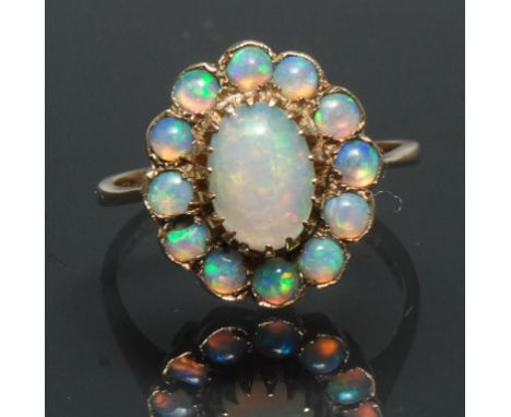 An opal cluster ring, central oval opal cabochon surrounded by a collar of twelve similar round cabochons, all flashing stron