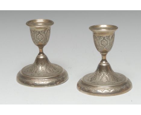 A pair of Iranian silver coloured metal candlesticks, chased in the typical Persian manner with stylised lotus, urnular sconc