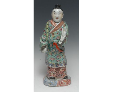 A Chinese porcelain figure, of a musician, he stands in flowing robes holding a bamboo flute, his other hand extended in a gr