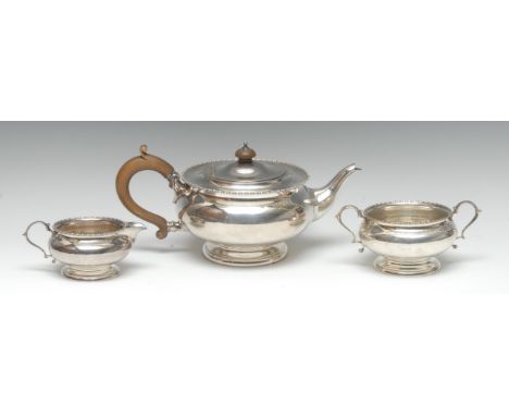 A George V silver three piece tea service, comprising teapot, milk jug and sugar basin, bead-and-reel borders, scroll-capped 