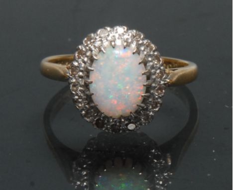 A diamond and opal cluster ring, central oval opal cabochon flashing vibrant red, green, blue and violet colours, surrounded 