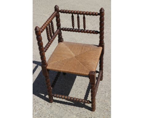 An early 20th century bobbin turned corner elbow chair with rush envelope seat 