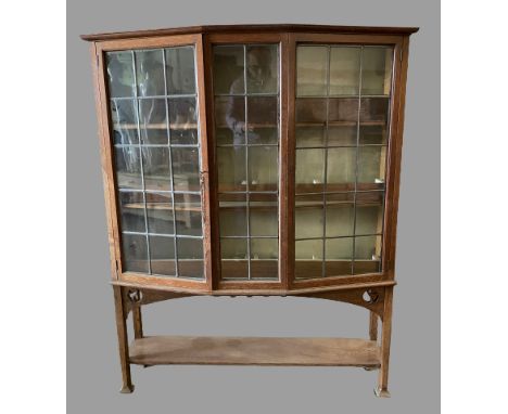 ARTS &amp; CRAFTS STYLE BOOKCASE CUPBOARD with angular bow front and leaded glass doors, 147cms H, 118cms W, 40cms D