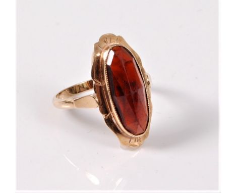 A 14ct garnet ring, the oval faceted garnet, approx. 16.3 x 6.5mm, in a collet mount and outer shaped border, to a plain band