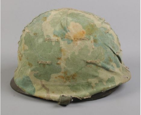 A vintage military helmet with camouflage cover and  broad arrow mark to inside; stamped 21 July 1961 to band.  