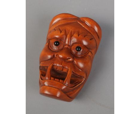 A Japanese carved Netsuke in the form of a Oni mask. Signed. Approx. length 5.5cm.  