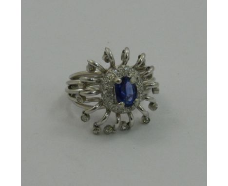 An unusual modern diamond and sapphire cluster ring, the central oval mixed cut sapphire in four claw setting on a raised dia