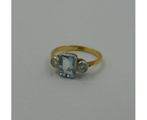 An 18 carat gold aquamarine and diamond three stone ring, the emerald cut aquamarine in millegrain rub-over setting between t