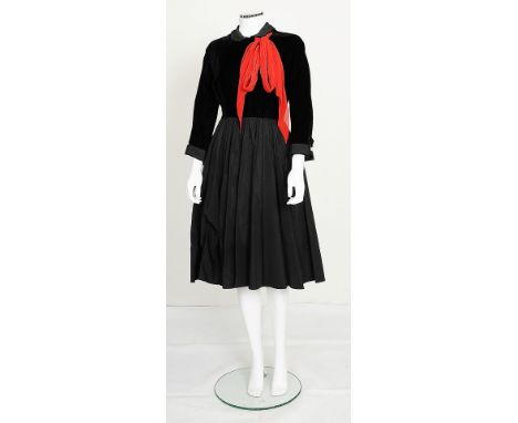 A 1950s black dress with striking red tie to neck, black velvet top with detailing to cuffs and neck, long sleeves, full crus