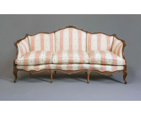 A LOUIS XVI STYLE WALNUT FRAMED SOFA of serpentine outline carved with flowers and scroll work and upholstered in a pale gree