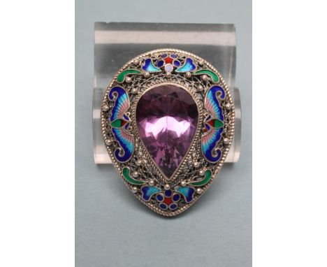 AN ENAMELLED BROOCH/PENDANT, the tear shaped filigree panel centred by a facet cut amethyst coloured stone within a border of