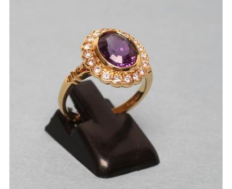 AN AMETHYST AND DIAMOND CLUSTER RING, the oval facet cut amethyst in a plain bezel and border of eighteen round brilliant cut