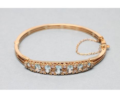 AN AQUAMARINE AND DIAMOND STIFF HINGED BANGLE, the upper section grain set with twenty one oval facet cut graduated aquamarin