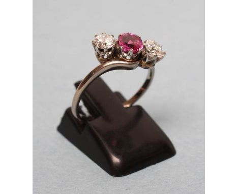 A THREE STONE RUBY AND DIAMOND CROSSOVER RING, the central ruby claw set and flanked by two brilliant cut diamonds to a plain