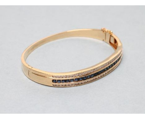 A SAPPHIRE AND DIAMOND STIFF HINGED BANGLE, the upper section channel set with a row of twenty six square cut sapphires withi