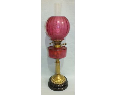 A Late-Victorian oil lamp, the cranberry glass reservoir on brass reeded column and stepped circular base, on black ceramic p