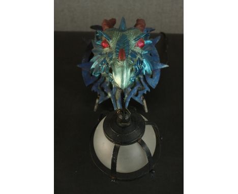 A moulded metallic painted dragon head wall lamp with caged frosted glass globe shade. H.33 W.23 D.23cm. 