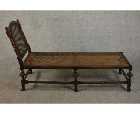 An early 20th century oak daybed in 17th century style, with a caned back and seat, the carved legs joined by stretchers. H.9