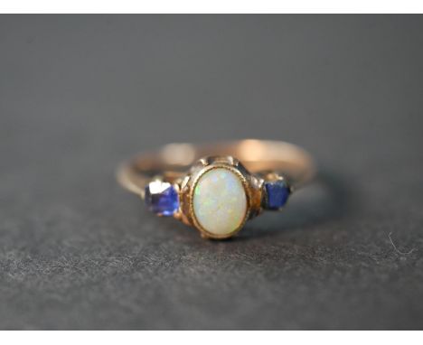 A pink metal (test as 9ct) opal and sapphire three stone ring, set to centre with an oval cabochon opal with an approximate c