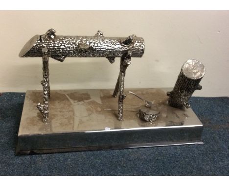 A large chrome moneybox in the form of a log on stand, mounted with an axe on rectangular base. Est. £50 - £80.