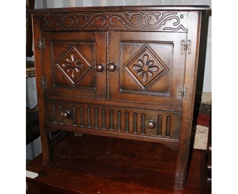 A Jacobean style oak hall unit, having two panelled doors and a drawer below, with a carved frieze, measuring 76cm high, 76cm