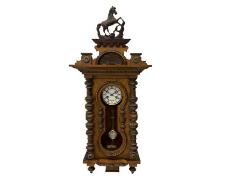 A late 19th century German wall clock in a mahogany case with a decorative carved pediment, full length shaped glazed door (g