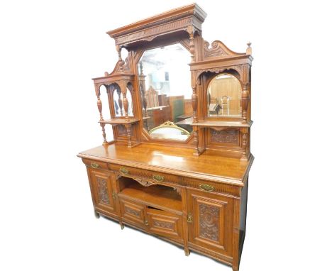 A late Victorian oak sideboard, the raised back with a central canted bevelled mirror plate, flanked by two arched plates and