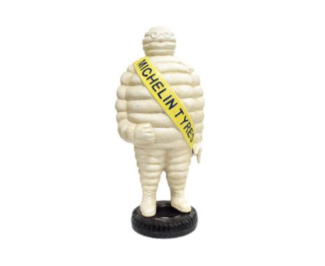 A Cast Metal Advertising Figure of the Michelin Man, wearing a yellow sash and standing on a black painted base in the form o