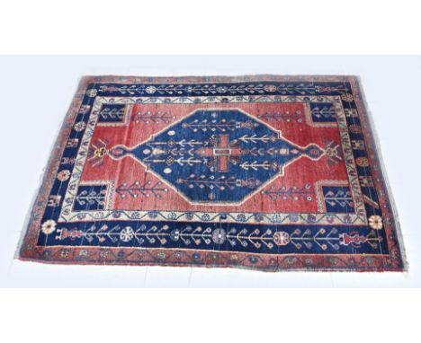 Hand knotted Persian carpet. Red in colour, with blue medallion and border. Dimensions: 190 x 128 cm. In good condition.