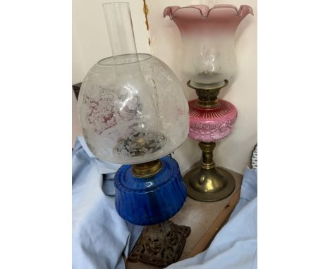 An oil lamp with a blue glass reservoir and cast base together with another oil lamp with a graded pink glass reservoir and g